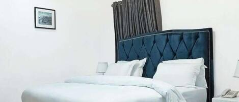 A modern bedroom with a large bed, a nightstand, a lamp, and a framed picture on the wall.
