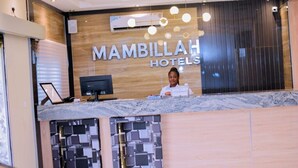 A reception desk at MambillaH Hotels with a modern design, a large screen, and a wooden panel wall.