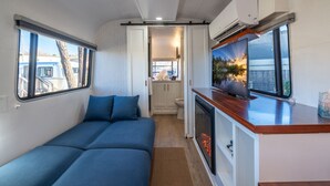 Interior de uma caravana compacta, com sofá, pequena cozinha e janela com vista para o exterior.