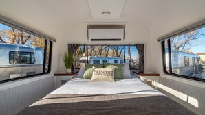 Quarto com cama, almofadas e janela com vista para um trem.