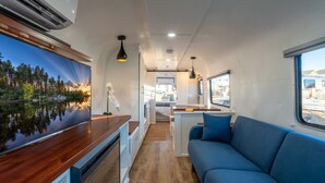 A compact RV interior with a kitchenette, a seating area, and a large window offering a scenic view. - Air Village Wagon Circle Unit #7 (Prescott)