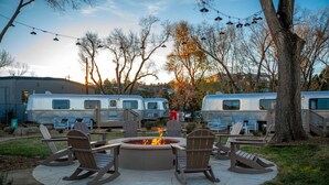 A fire pit with chairs and a dining table in a courtyard with RVs in the background.