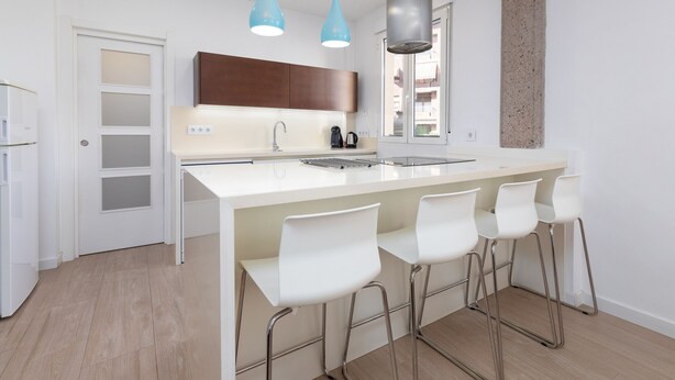 Una cocina moderna con una isla central, taburetes de bar, horno empotrado e iluminación colgante.