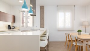 Una cocina moderna con armarios blancos, una isla central y un comedor con sillas y mesa de madera.