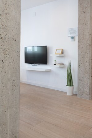 Una sala de estar moderna con un televisor de pantalla plana montado en una pared blanca, un estante con adornos y una planta en maceta.