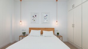 Un dormitorio con una cama grande, dos mesitas de noche con plantas, un cabecero de madera y dos lámparas fijadas a la pared.