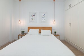 Un dormitorio minimalista con una cama grande, cabecera de madera, dos mesitas de noche con plantas y un armario.