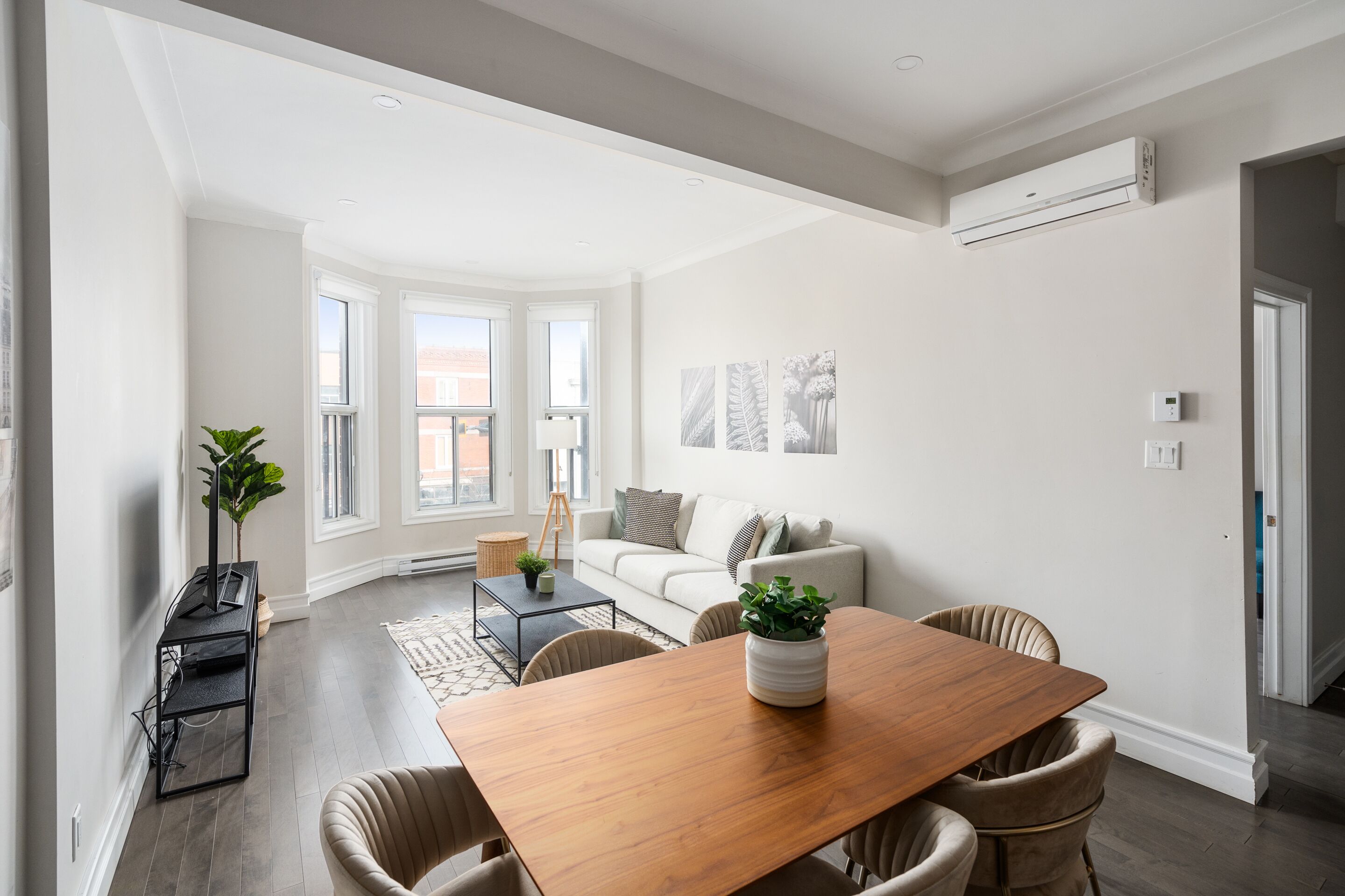 A modern living room with a wooden dining table, comfortable seating, a sofa, and a large window.