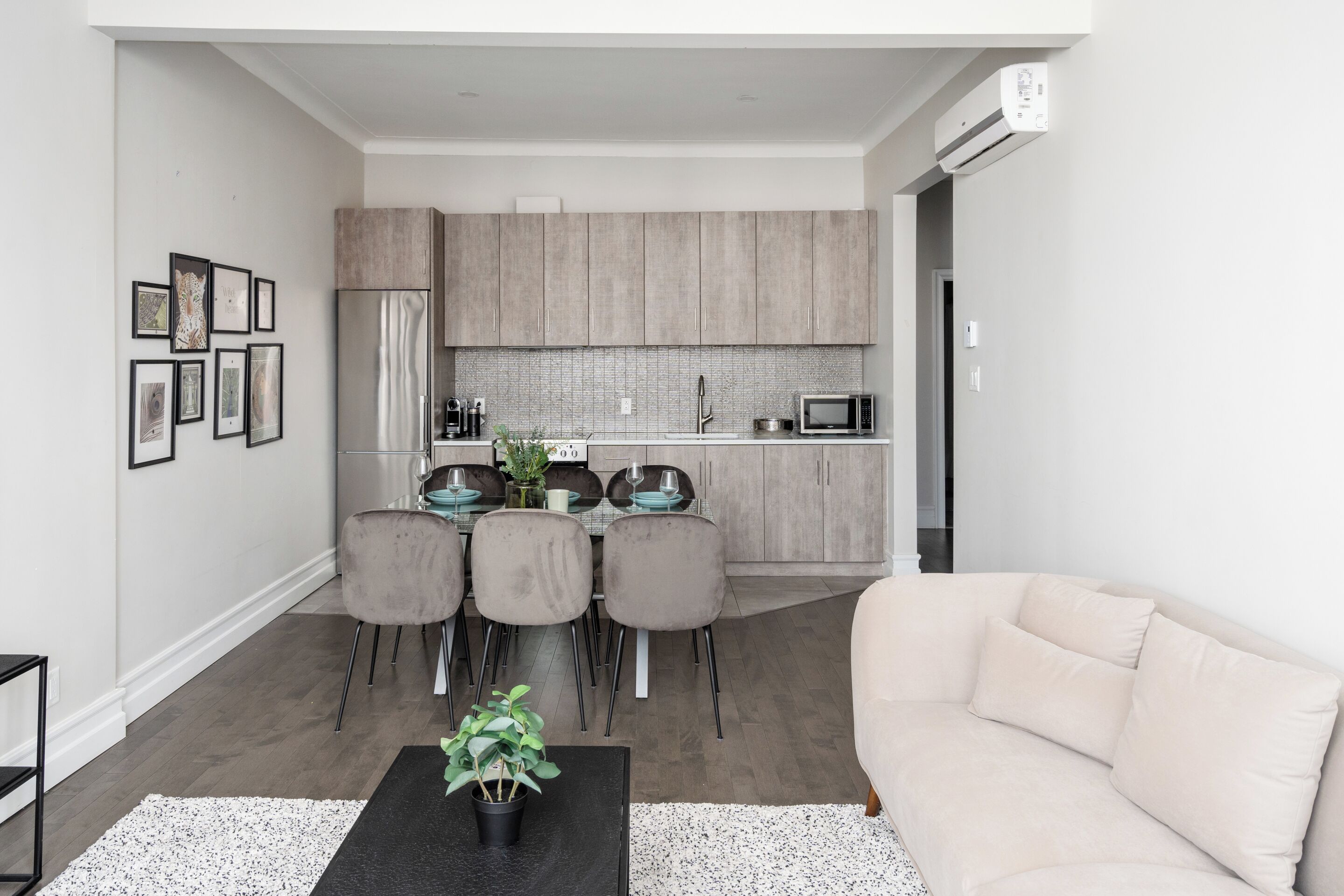 Ein modernes Wohnzimmer mit einem beigen Sofa, einem schwarzen Couchtisch und einem Essbereich mit einem Glastisch und Stühlen.