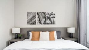 A modern bedroom with a large bed, two bedside tables with lamps, a small plant, and a wall-mounted artwork. - Plateau Prime Residence (Montreal)