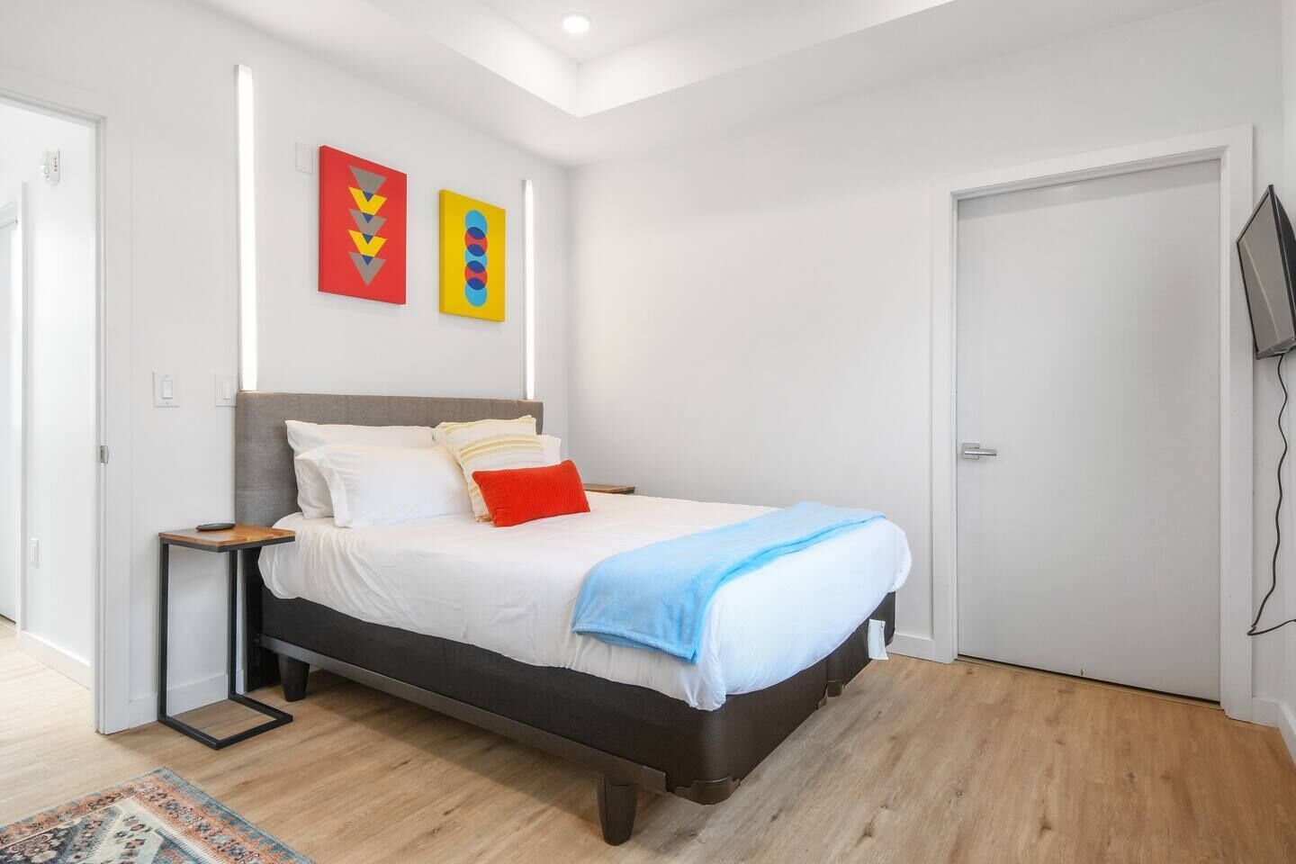 Une chambre à coucher moderne avec un lit, une table de chevet et un téléviseur fixé au mur.