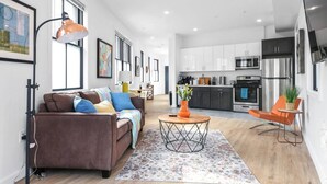 A modern living room with a brown sofa, a coffee table, and a kitchen in the background. - ✮Unique 1BR | Walk to NJPAC/NJPENN | 30min to NYC✮ (Newark)