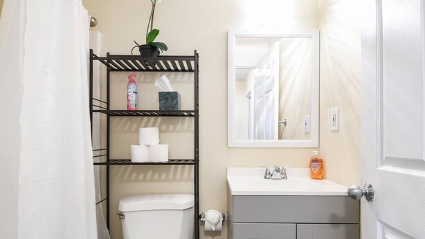 Un baño pequeño con inodoro, estante con artículos de tocador, lavamanos y espejo.