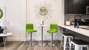 Een moderne keuken met twee groene barkrukken, een ronde tafel en een decoratieve zonneslinger spiegel.