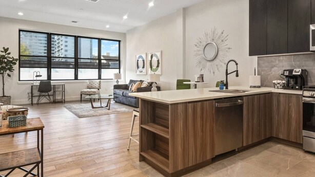 Een moderne keuken met een centraal eiland, donkere kastjes en een groot raam dat voor natuurlijk licht zorgt.