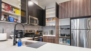 Een moderne keuken met donkere houten kastjes, roestvrijstalen apparatuur en geordende planken met keukengerei.
