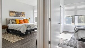Une chambre à coucher avec un lit, une table de chevet, un tableau et une fenêtre avec des stores.