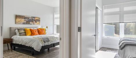 Un dormitorio con cama, mesita de noche, un cuadro y ventana con persianas.