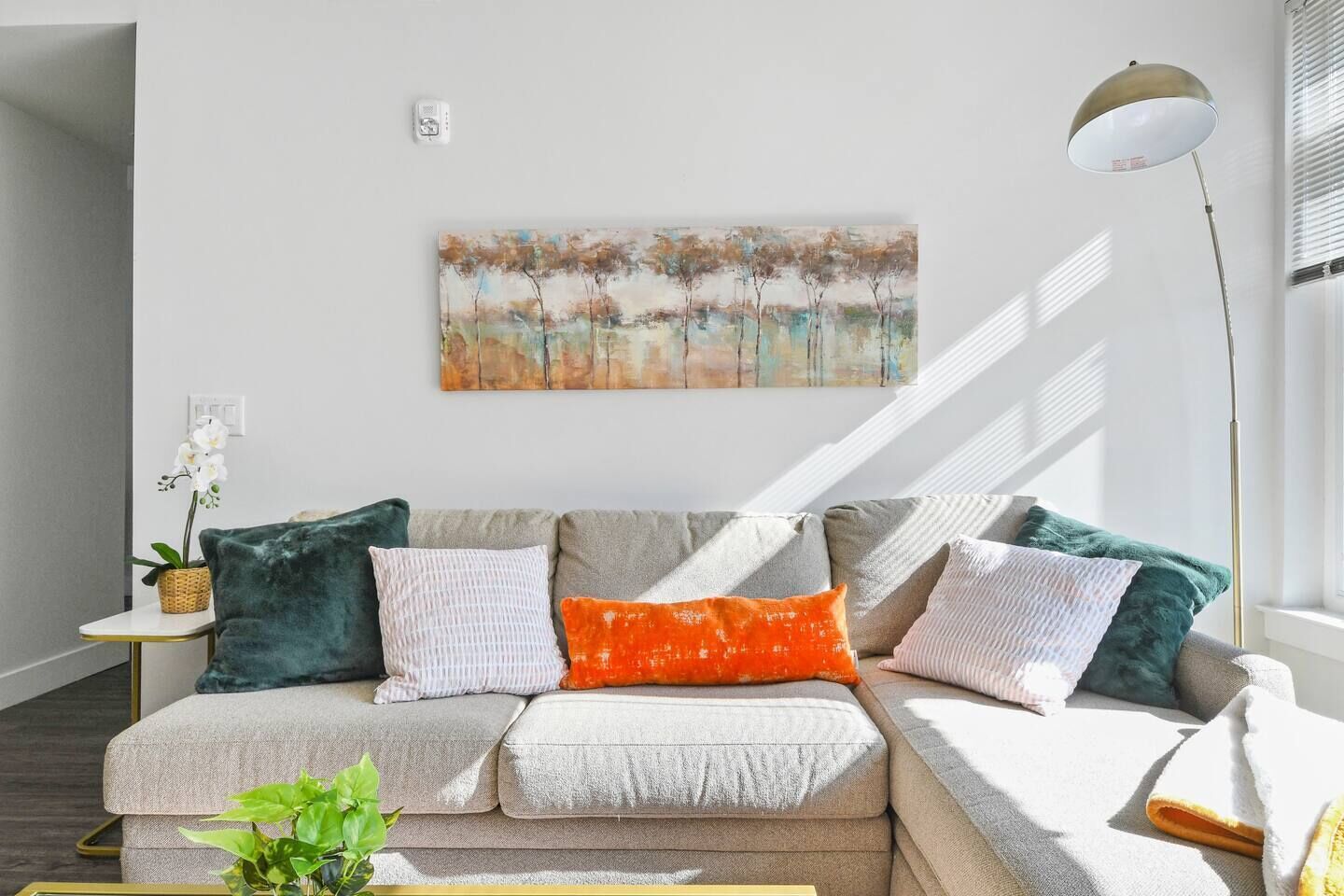 A modern living room with a sectional sofa, a floor lamp, and a painting on the wall.