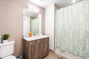 Un baño con lavamanos blanco, tocador de madera y cortina de ducha con diseño geométrico.