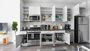 Une cuisine moderne avec des meubles blancs, un réfrigérateur en acier inoxydable, un four à micro-ondes, une cuisinière et des étagères ouvertes où sont rangés divers ustensiles de cuisine.