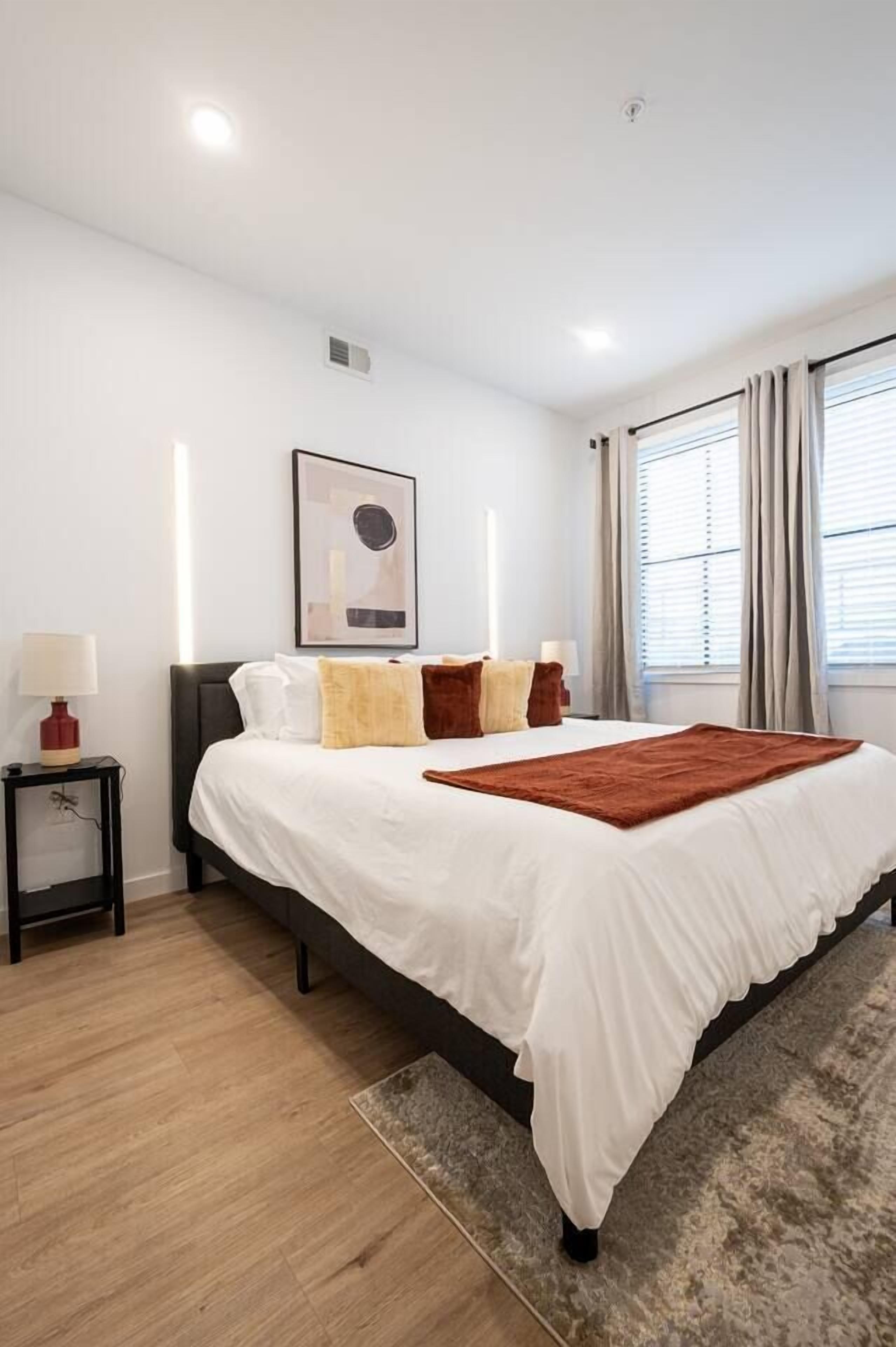 Une chambre à coucher moderne avec un grand lit, une table de chevet, une commode et une fenêtre avec des rideaux.