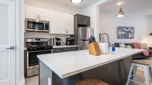 A modern kitchen with white cabinetry, stainless steel appliances, and a central island with stools. - Sleek ! 1BR King ! 30 min to NYC (newark)