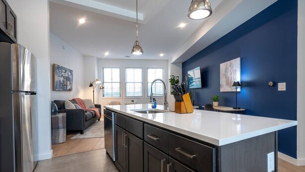 A modern kitchen with a large island, dark cabinetry, and stainless steel appliances. - Sleek ! 1BR King ! 30 min to NYC (newark)