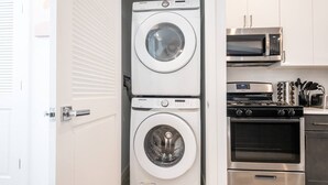 A compact kitchen with a microwave, oven, and stacked washer-dryer unit. - Sleek ! 1BR King ! 30 min to NYC (newark)