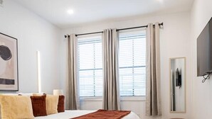 A modern bedroom with a large bed, a TV, and a small stool. - Sleek ! 1BR King ! 30 min to NYC (newark)