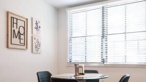 A modern dining area with a round table and four chairs, a window with blinds, and framed artwork on the wall. - Sleek ! 1BR King ! 30 min to NYC (newark)