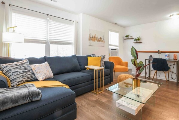 Ett modernt vardagsrum med en mörkblå soffa, ett soffbord i glas och en orange fåtölj.