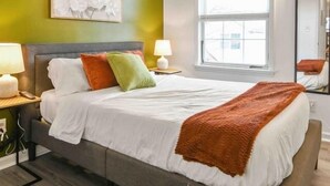 A modern bedroom with a bed, green walls, a large window, and a mirror. - Lavish 3Bed Apt !  Free Gated Parking! 30 min NYC! (newark)