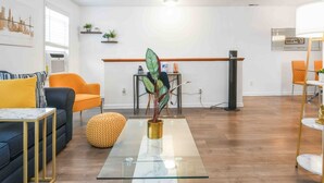 A modern living room with a sofa, armchair, and ottoman, a glass coffee table, and a dining area with chairs and a table. - Lavish 3Bed Apt !  Free Gated Parking! 30 min NYC! (newark)