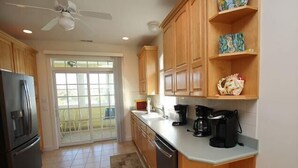 A kitchen with wooden cabinets, a refrigerator, a coffee maker, and a sliding glass door leading to a balcony. - Immaculately maintained property just steps to the beach in Dewey Beach. (Dewey Beach)