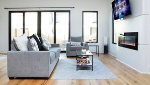 A modern living room with a grey sofa, a coffee table with books, a fireplace, and a TV mounted on the wall. - Newly Built Modern Home In CLT! Great Location! (Charlotte)