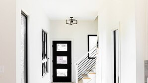 A hallway with wooden flooring, white walls, and a black door with glass panels. - Newly Built Modern Home In CLT! Great Location! (Charlotte)