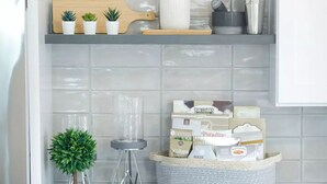 A kitchen with white tiled walls, shelves with plants, a cutting board, a blender, and a basket of groceries. - Newly Built Modern Home In CLT! Great Location! (Charlotte)