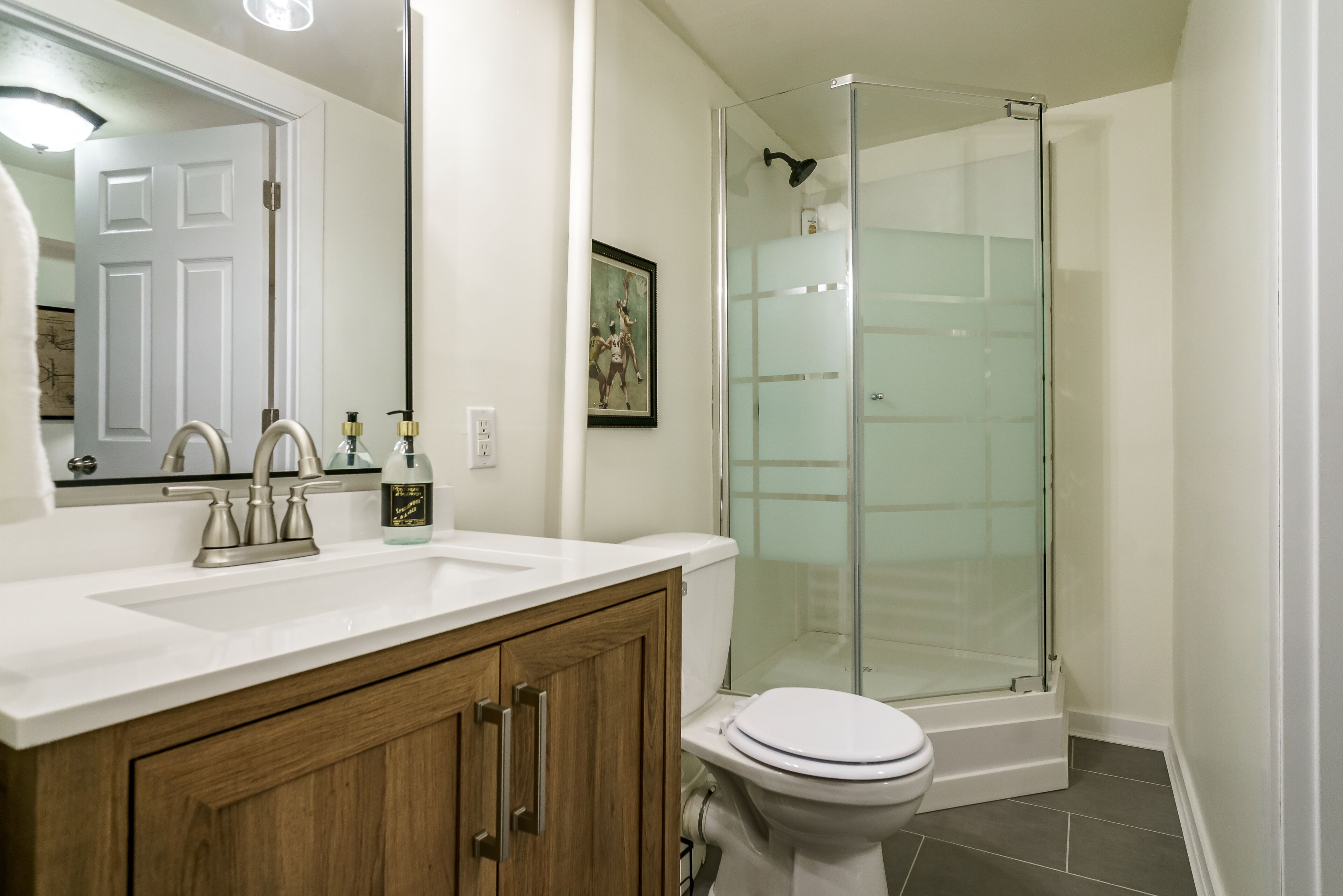 Une salle de bain avec un lavabo blanc, des meubles en bois, des toilettes et une douche à parois de verre.
