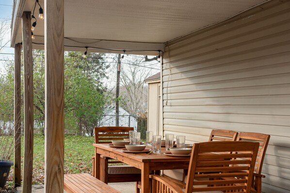 A wooden table set for four with chairs, a bench, and a covered patio area with string lights.