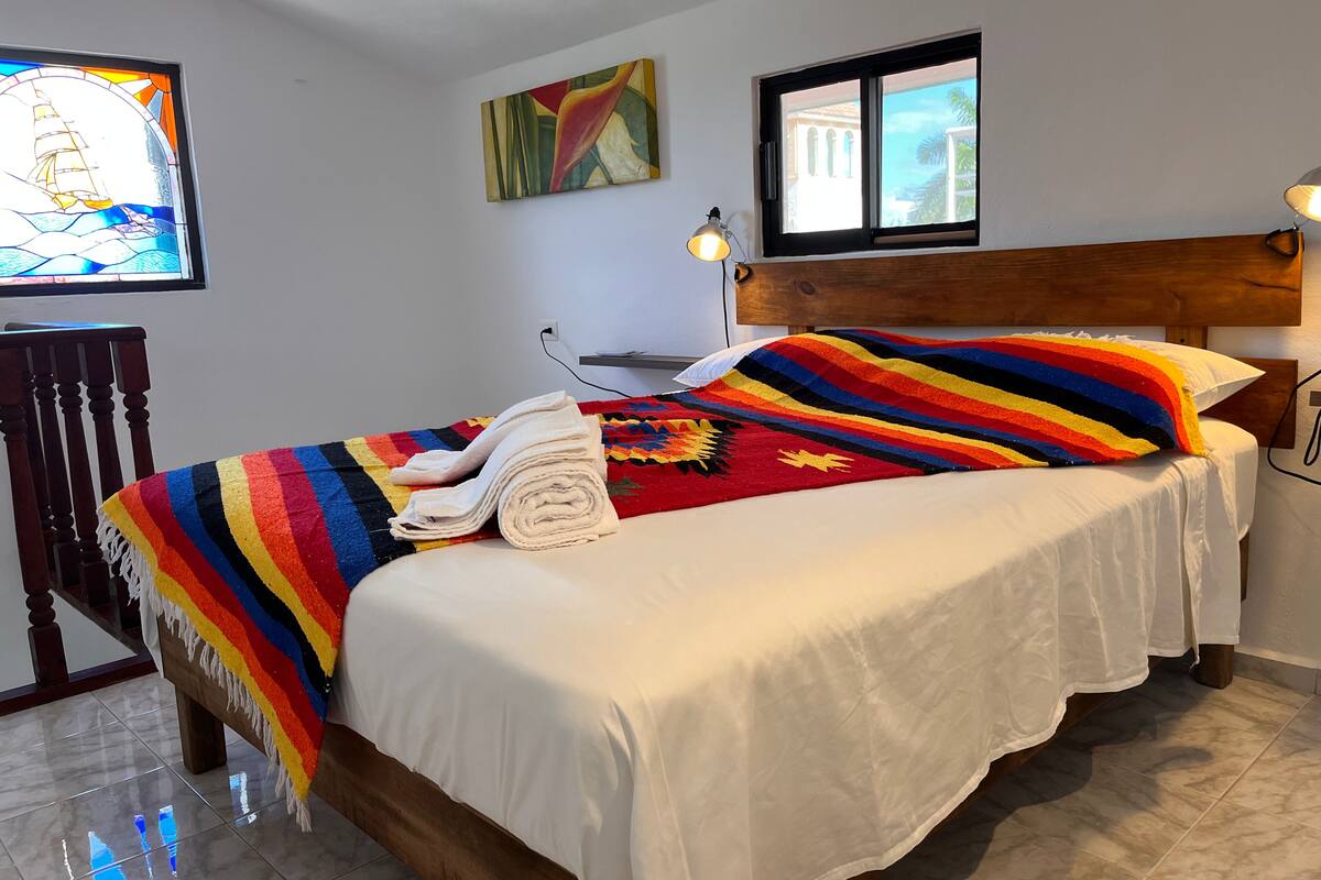 Ein Schlafzimmer mit einem Bett, einem Sessel, einem Gemälde, einem Fenster und einer Lampe.
