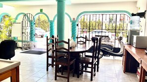 Un espace repas avec une table ronde et des chaises, un distributeur d’eau et une vue sur les voitures garées à l’extérieur.