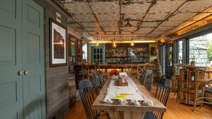 Un comedor rústico con una larga mesa de madera, sillas y una zona de bar con estantes y botellas.
