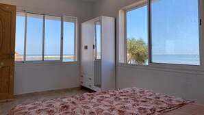 Une chambre avec un lit, une armoire et de grandes fenêtres donnant sur la plage.