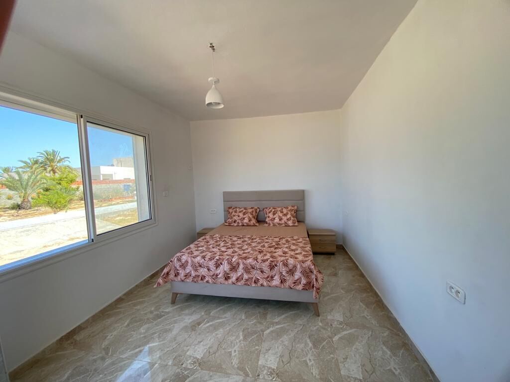 Ein Schlafzimmer mit Bett, Nachttisch, Fenster und Deckenleuchte.