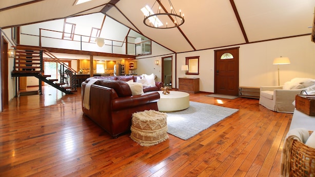 Un loft spacieux doté d’un plancher en bois, d’un canapé en cuir marron, d’une table basse ronde blanche et d’un escalier menant à un niveau supérieur.