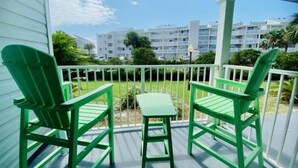Un balcón con dos sillas Adirondack verdes y una pequeña mesa, con vistas a una zona ajardinada y un edificio de varios pisos.