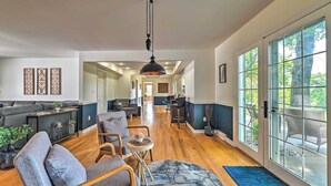 A spacious living area with a sofa, chairs, and a dining table. There are large windows with a view of the outdoors.