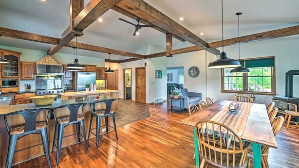 A spacious kitchen with wooden beams, a dining area with a large wooden table, and a bar with stools.