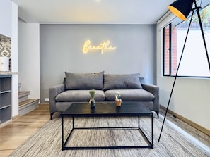 Een moderne woonkamer met een grijze bank, een zwarte salontafel en een neonbord waarop staat 